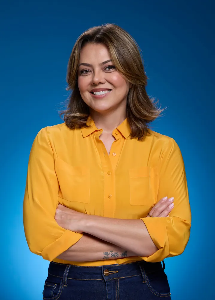 Retrato da senadora Leila do Vôlei de braços cruzados, camisa amarela, fundo azul